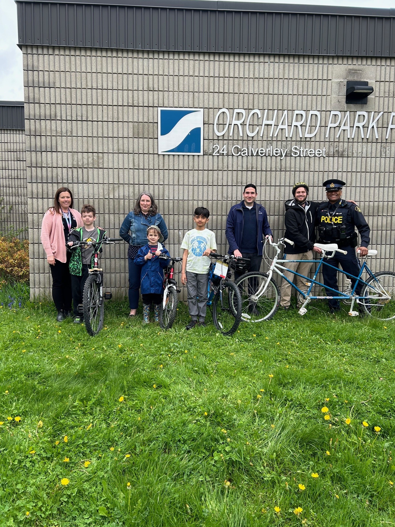 Adults and children with bikes standing in front the Orchard Park Public School sign
