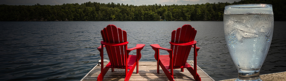 Two Muskoka chairs on a dock with a glass of water