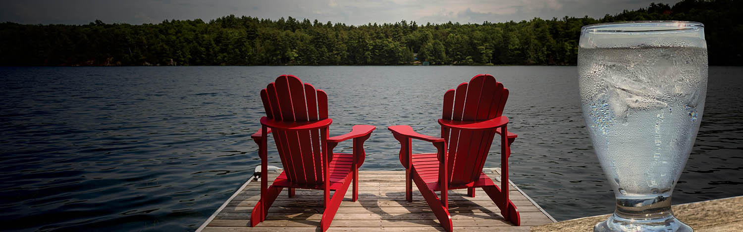 two red Muskoka chairs on a dock with a glass of water